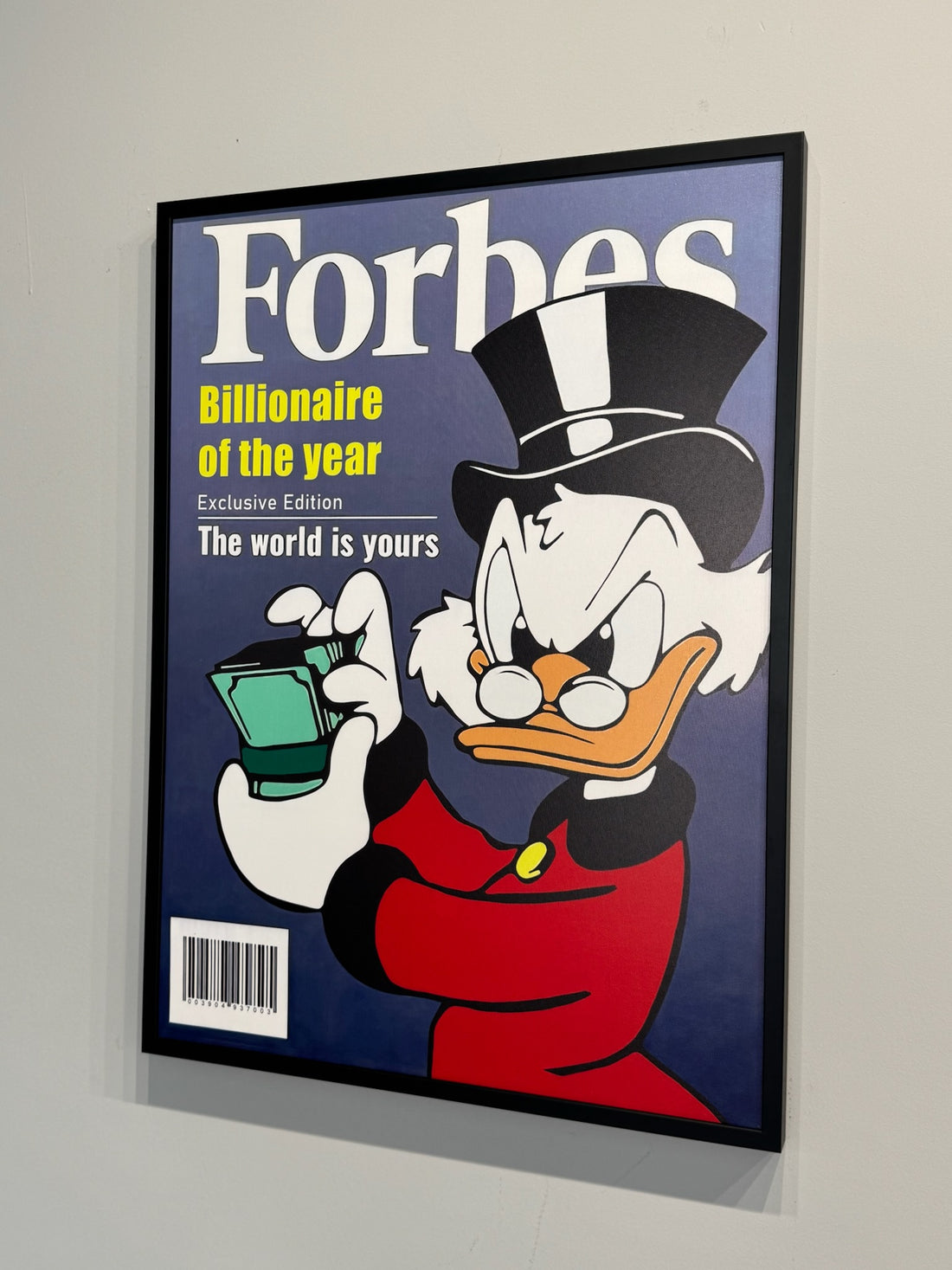 Framed poster of a cartoon character holding money with 'Forbes' branding on a gray wall.