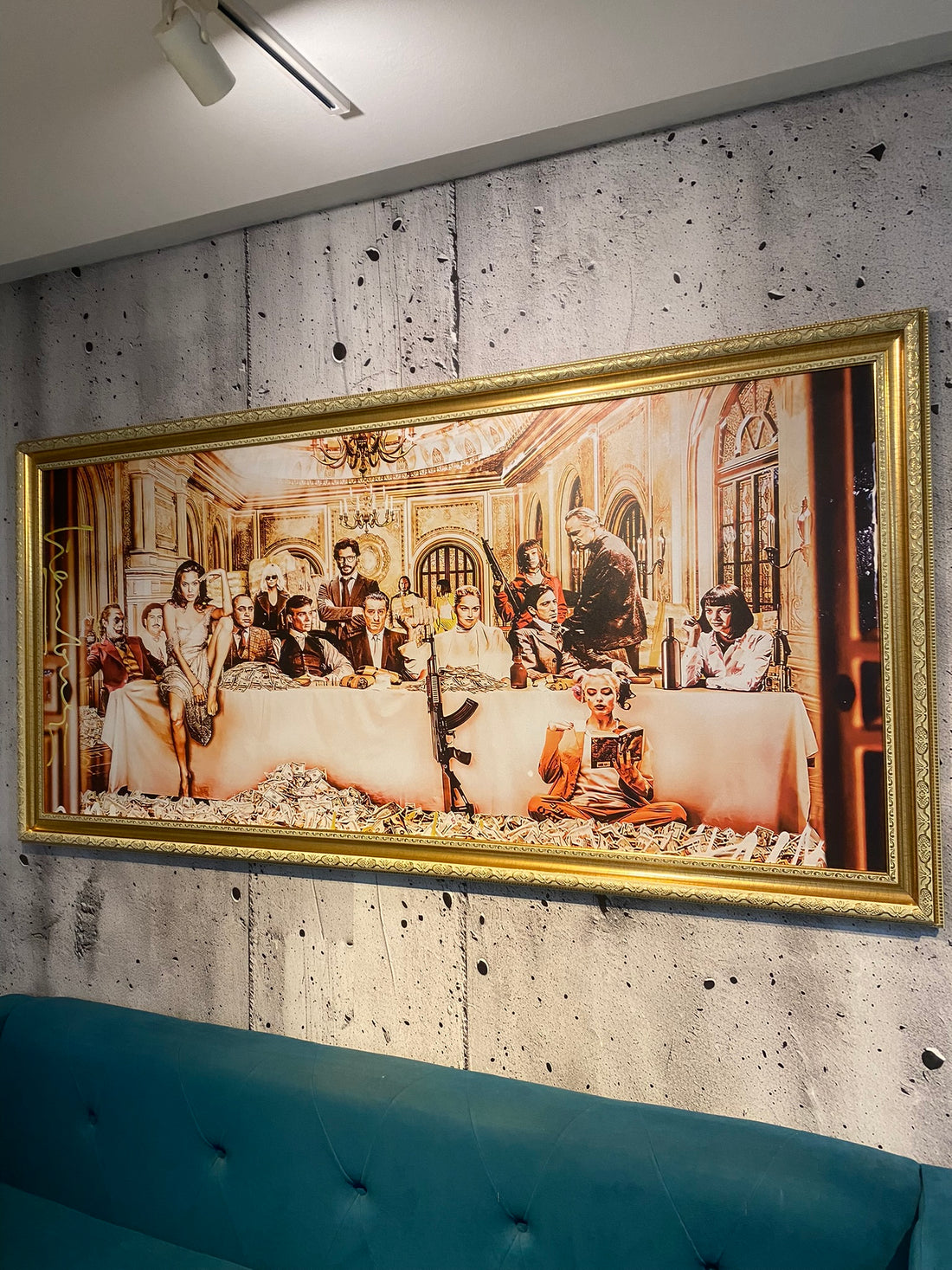 Framed artwork of a group scene on a textured wall above a blue sofa.
