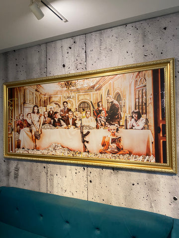 Framed artwork of a group scene on a textured wall above a blue sofa.