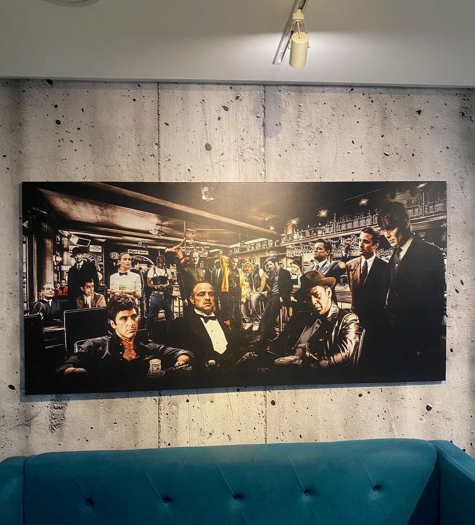 Large black and white painting of a crowded room on a concrete wall above a blue sofa.