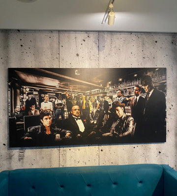 Large black and white painting of a crowded room on a concrete wall above a blue sofa.