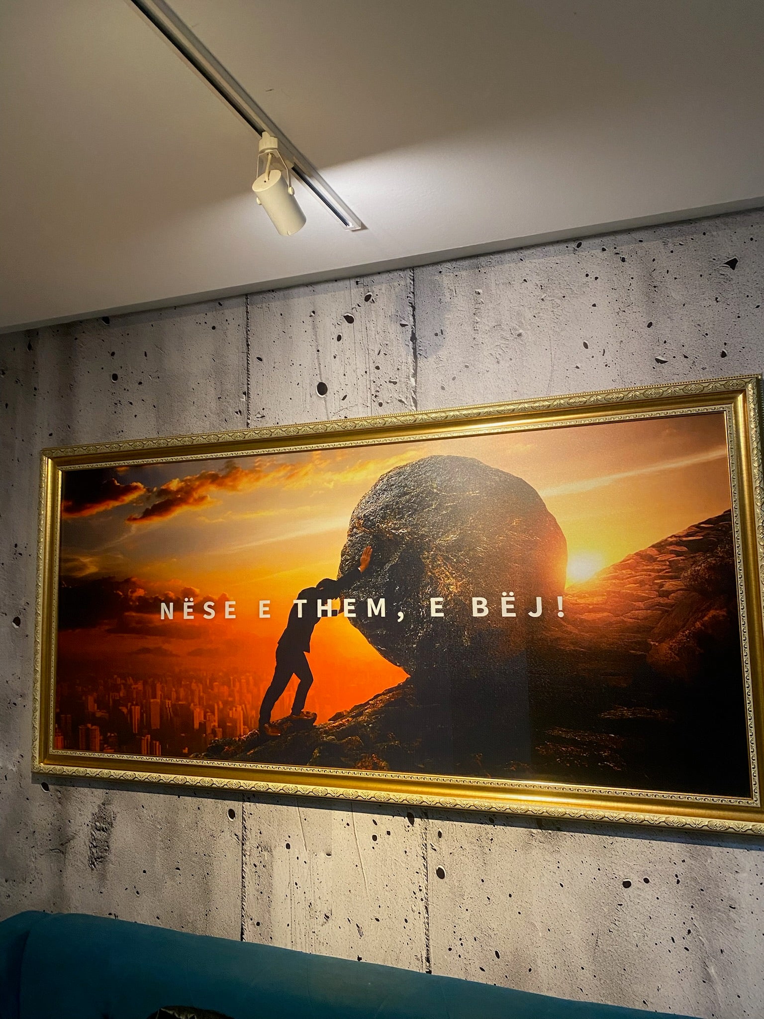 Framed artwork of a silhouette against a sunset with text on a textured wall.