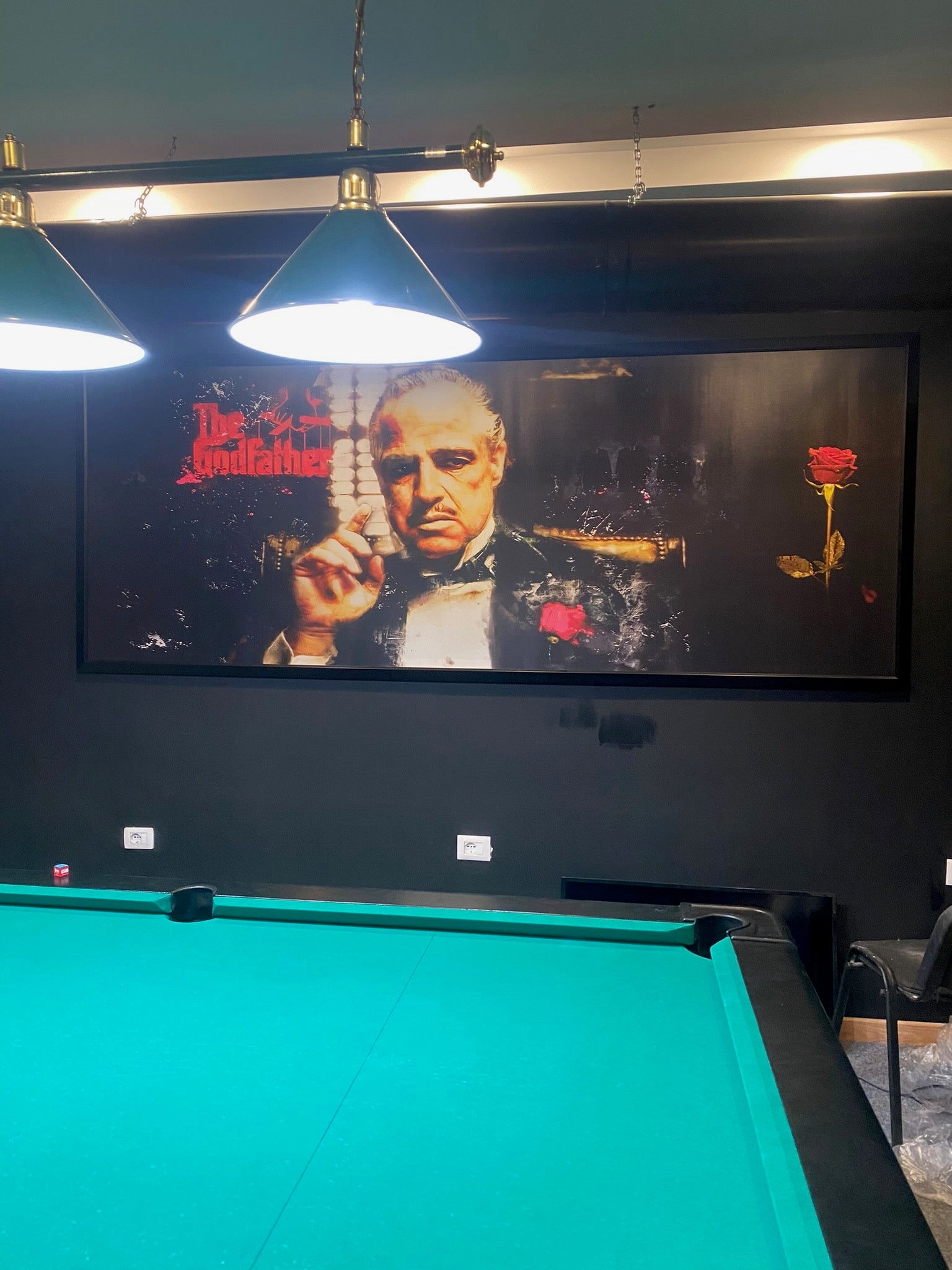 Pool table with a movie screen displaying 'The Godfather' in a room.