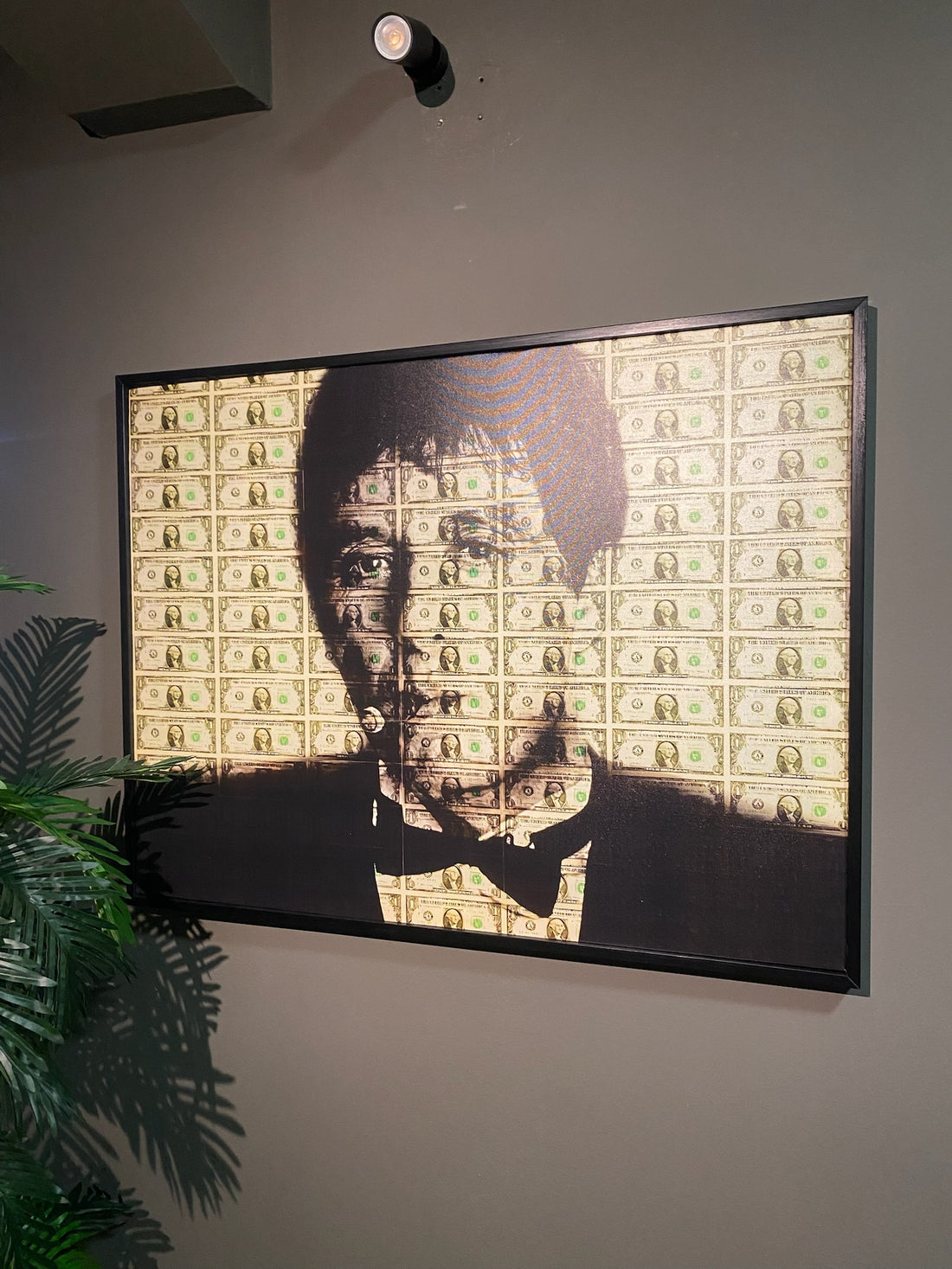 Framed artwork of a portrait with dollar bill pattern on a wall.