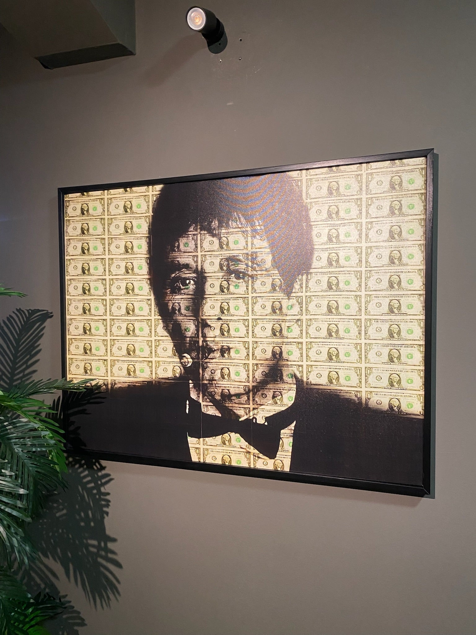 Framed artwork of a portrait with dollar bill pattern on a wall.