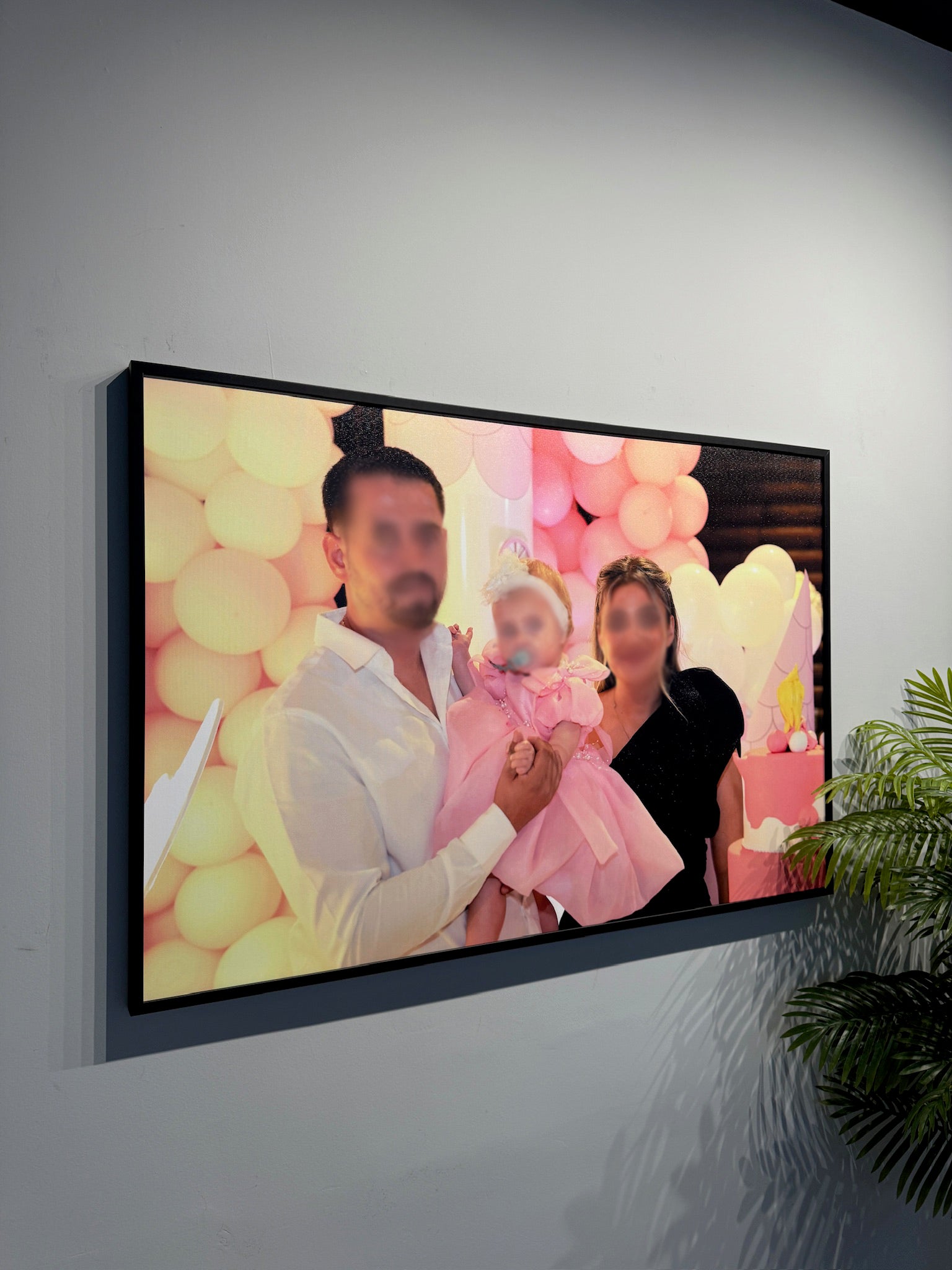 Framed photograph of a family with balloons and a cake on a wall.