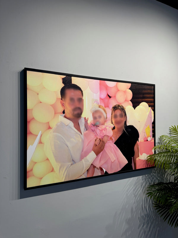 Framed photograph of a family with balloons and a cake on a wall.
