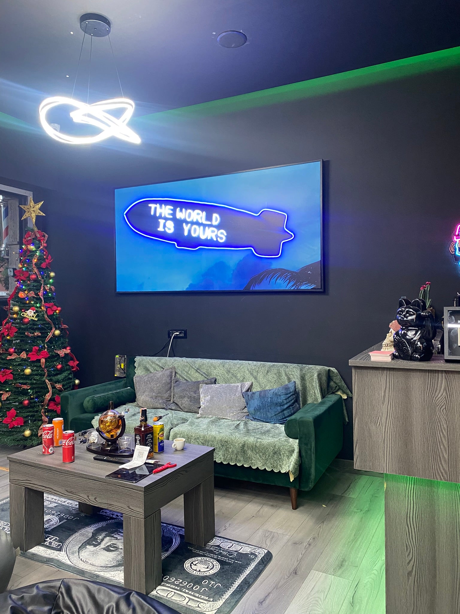 Modern living room with a green couch, coffee table, and wall-mounted TV displaying 'The World is Yours'.