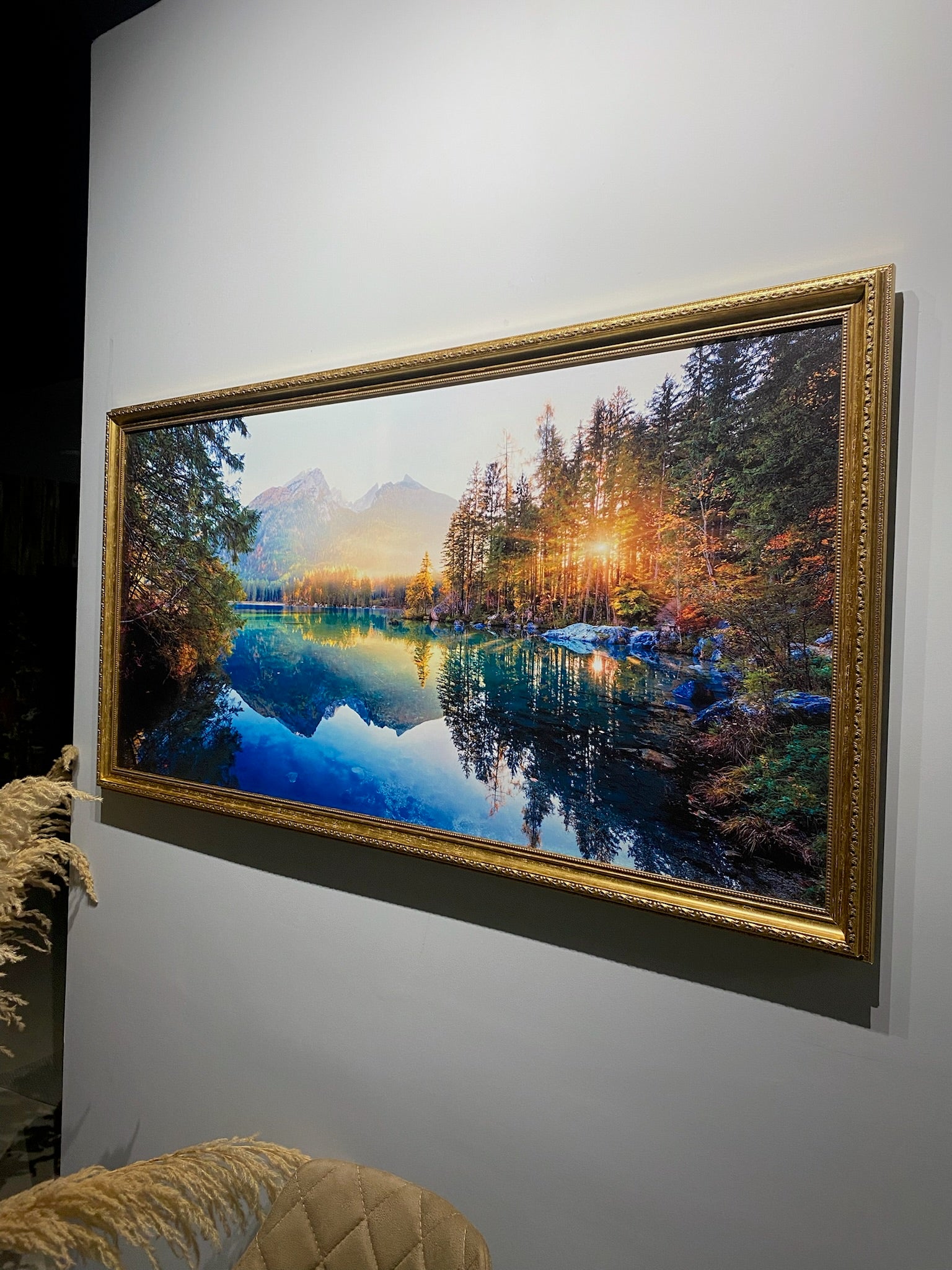Framed landscape painting of a lake and trees on a wall.