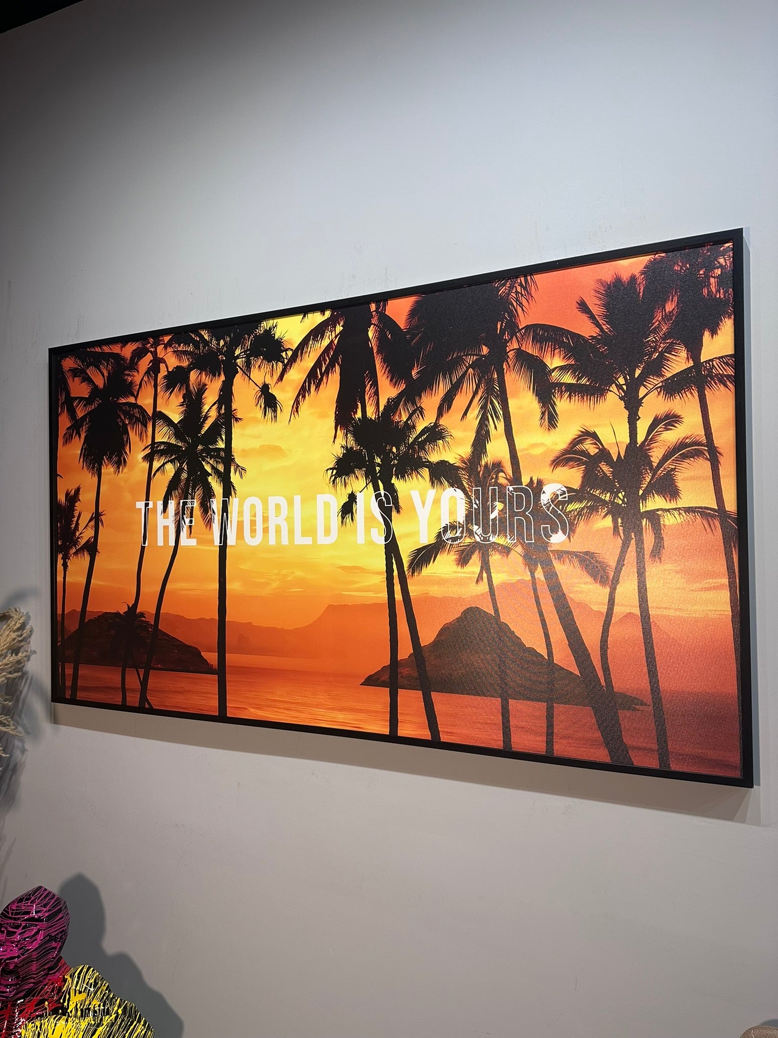 Framed artwork with palm trees and 'The World is Yours' text against a sunset background.