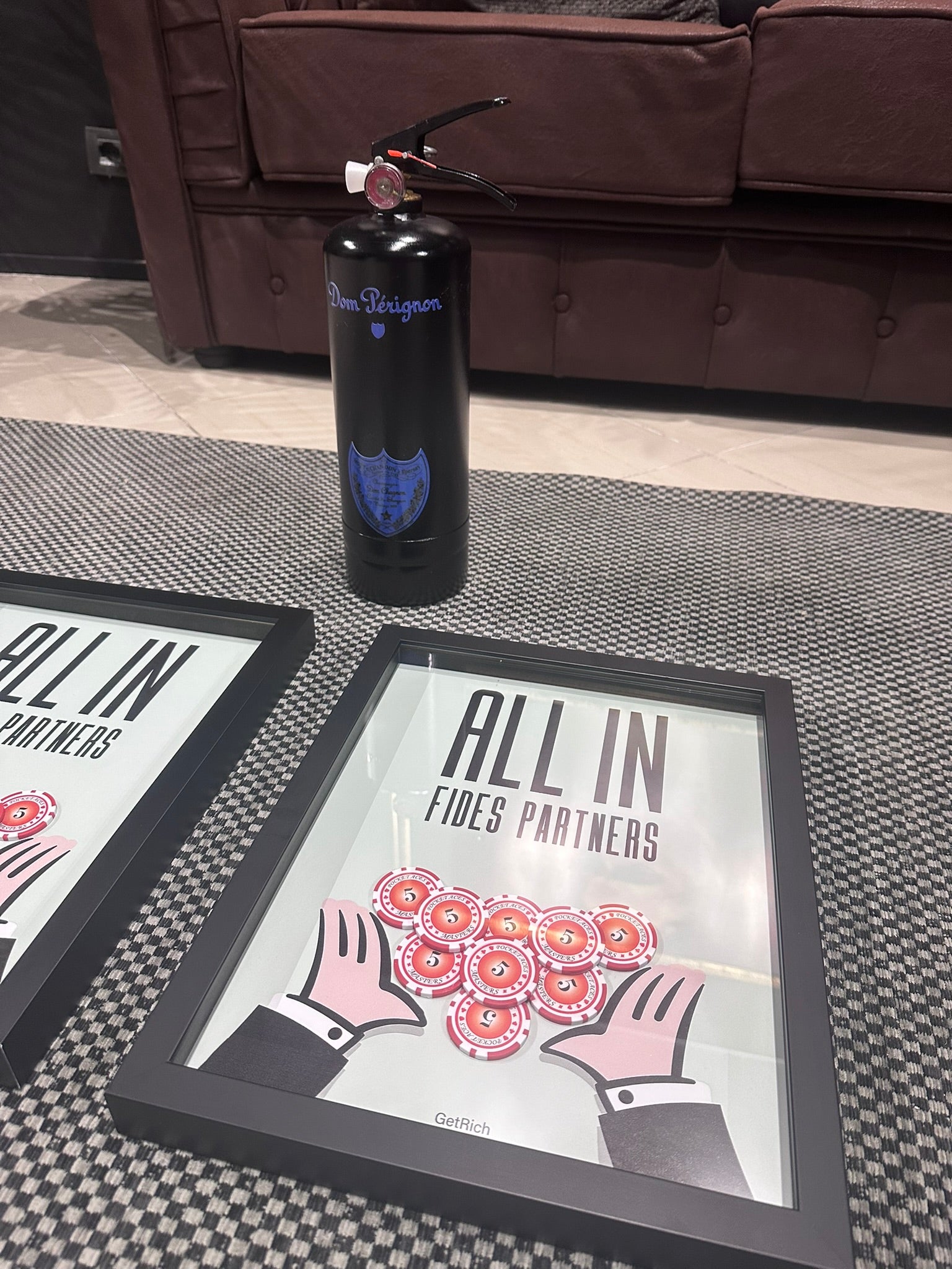 Framed posters with 'All In Fides Partners' text and graphic design on a checkered floor.