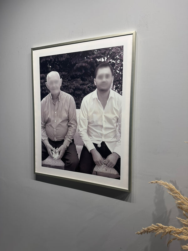 Framed black and white photograph of two people sitting side by side on a gray wall.