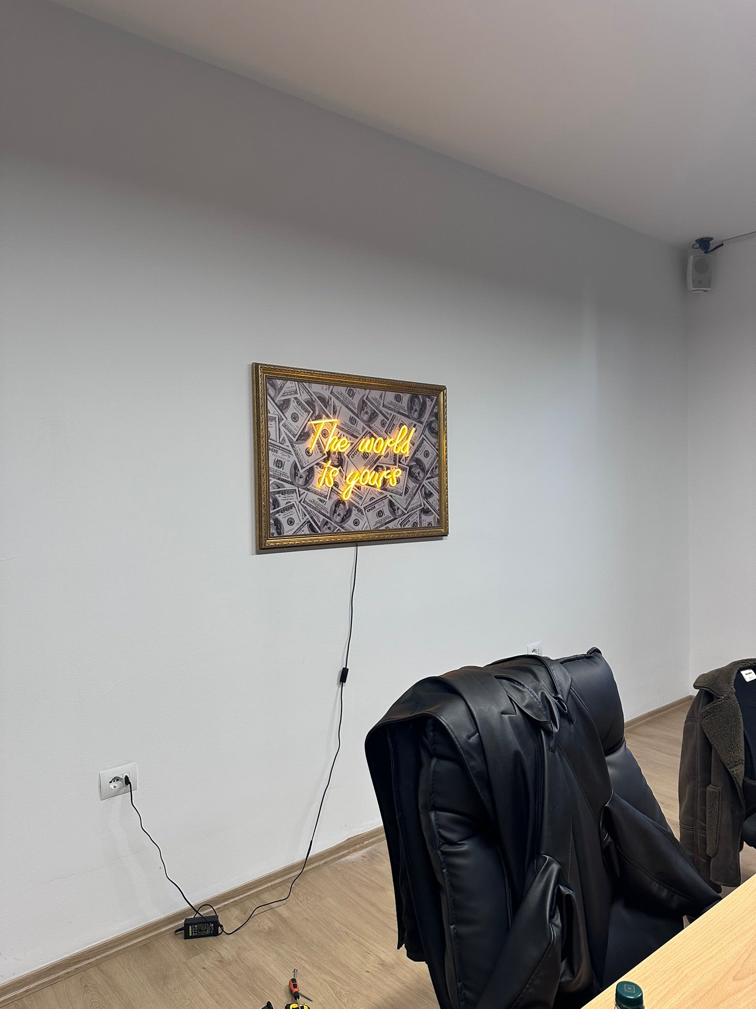 Neon sign on a wall with coats hanging below in a room.