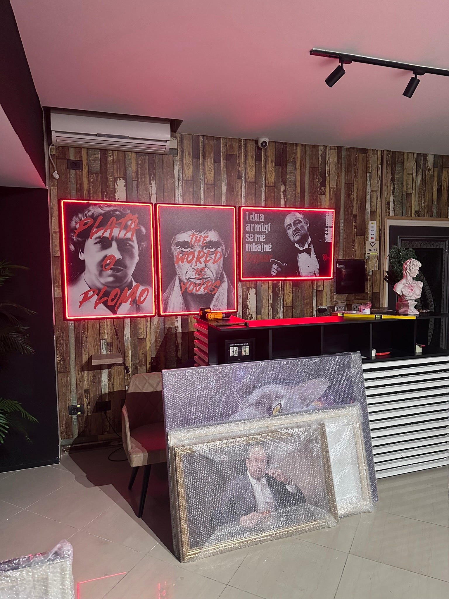 Neon signs and framed pictures on a wall with a decorative pattern.