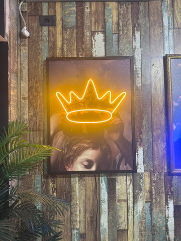 Neon crown light fixture on a wooden wall with a blurred portrait below.