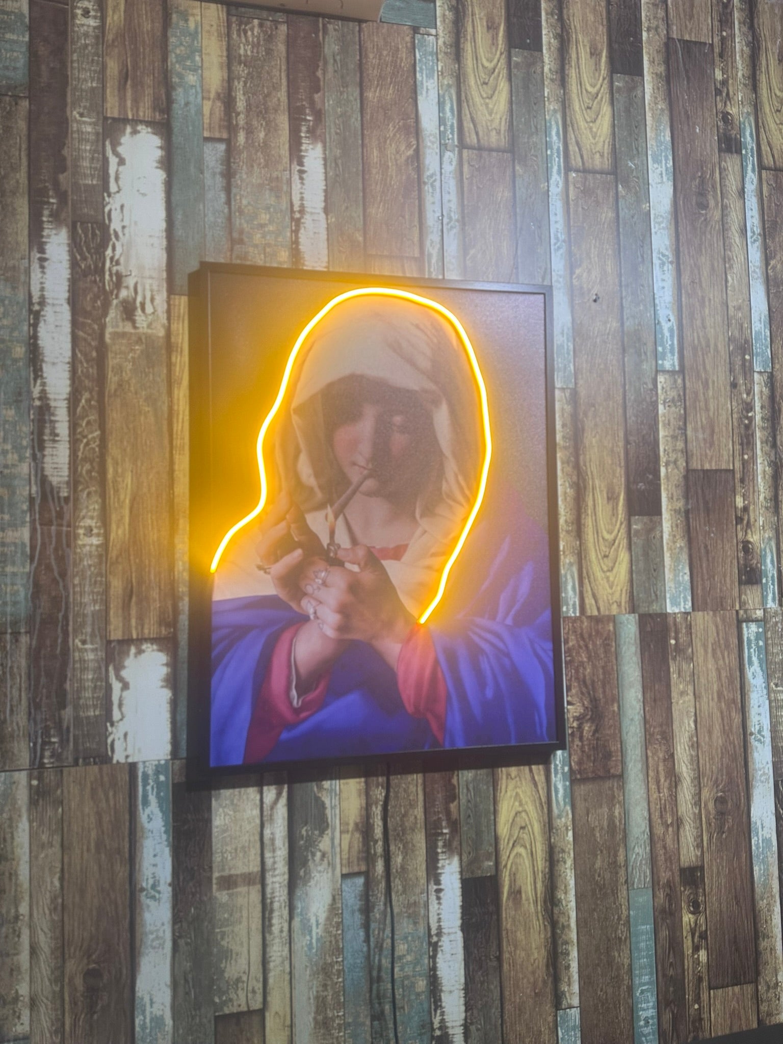 Neon light art of a religious figure on a wooden wall.