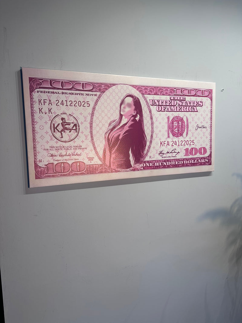 Framed print of a $100 bill with a portrait on a plain wall.