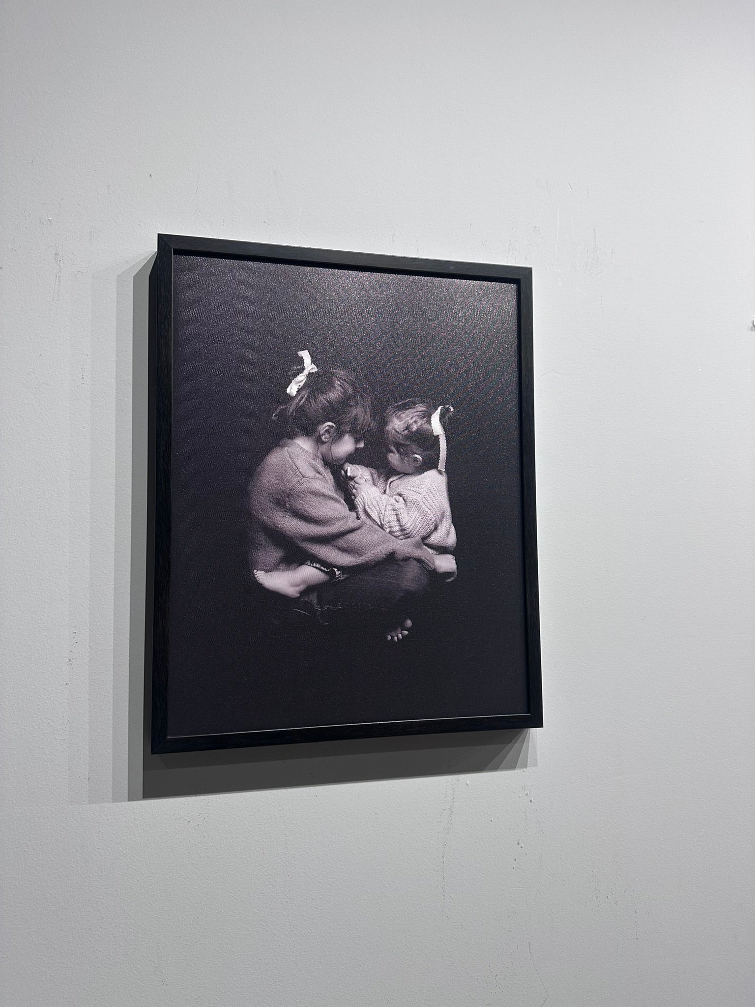 Framed black and white photograph of two people embracing on a white wall.