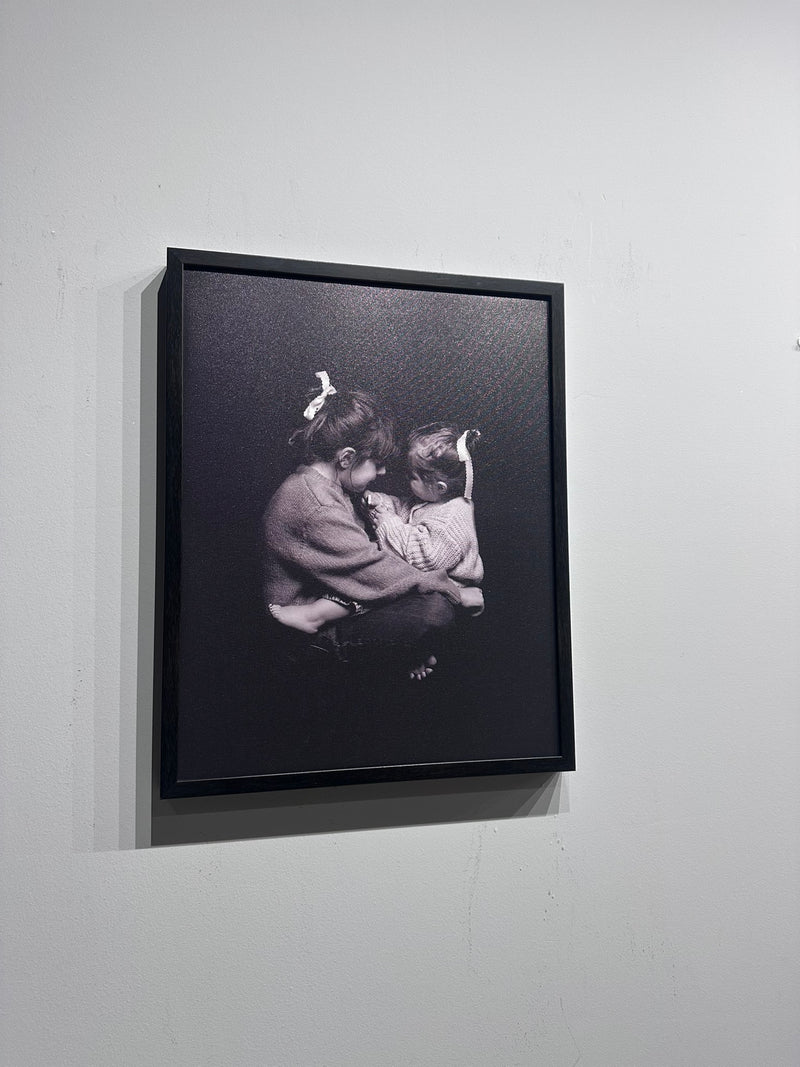 Framed black and white photograph of two people embracing on a white wall.