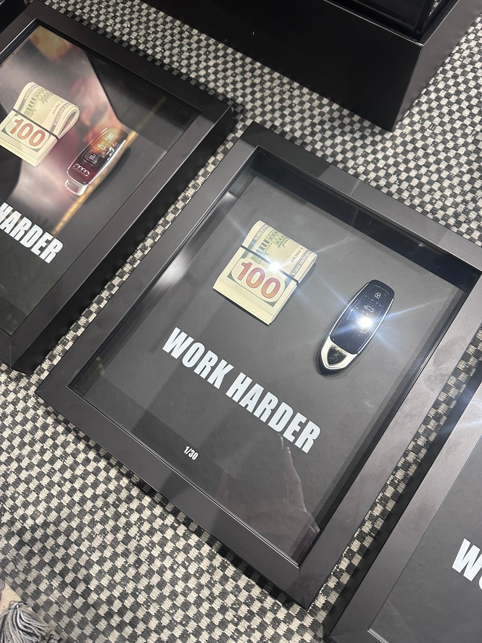 Framed motivational quote 'Work Harder' with a gold coin and key on a checkered background.