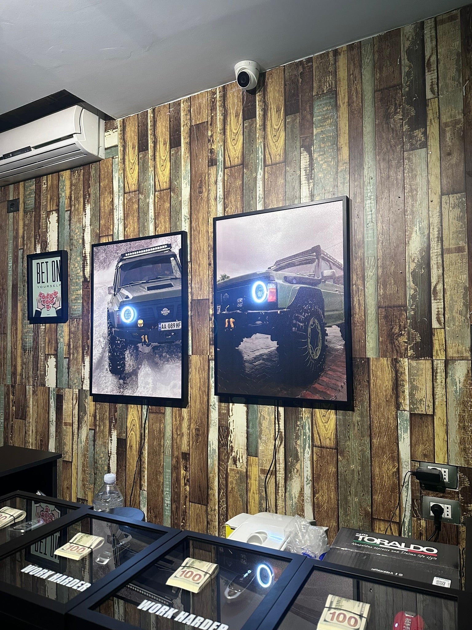 Wooden wall with framed pictures of vehicles, air conditioner, and display case.