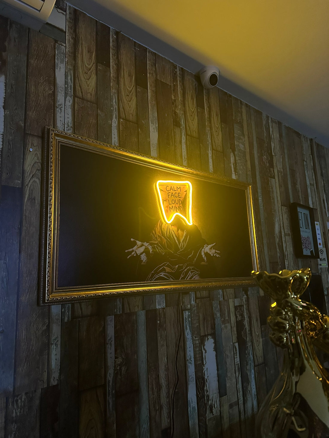 Neon sign with a face design on a framed artwork against a wooden wall.