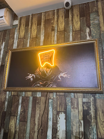 Neon sign with a face design on a framed artwork against a wooden wall.