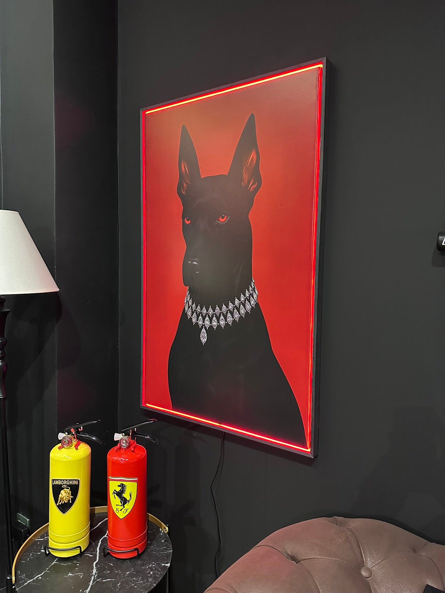 Framed artwork of a black dog with a red background on a dark wall, next to two fire extinguishers.