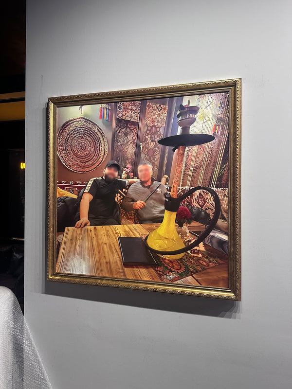 Framed picture of two men with a hookah on a wooden table.