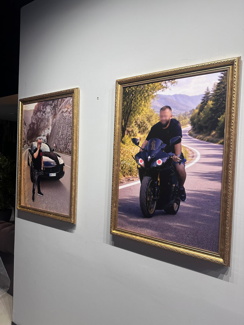 Two framed photographs on a wall, one of a person by a car and the other of a person on a motorcycle.