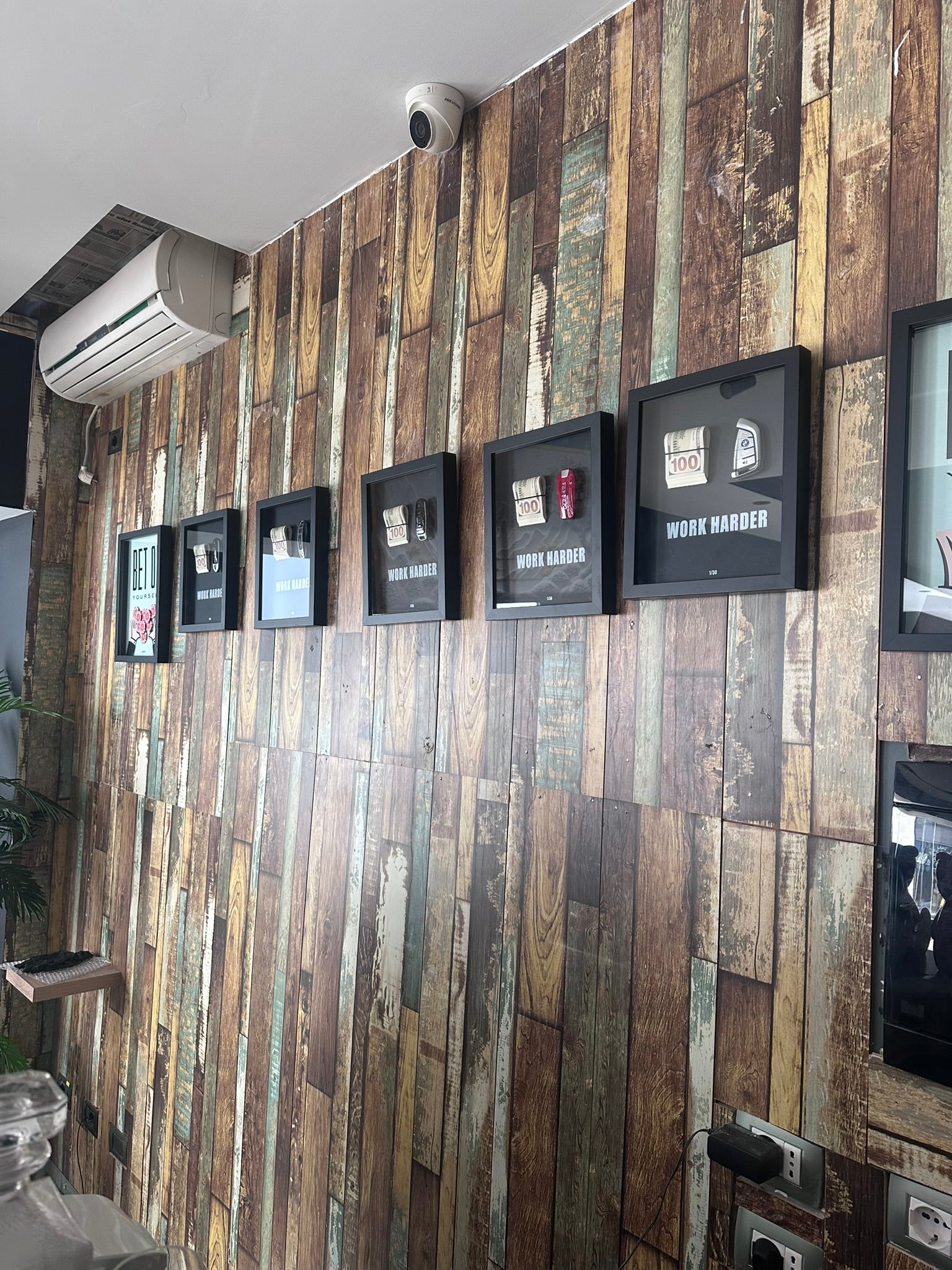 Wooden panel wall with framed pictures and a camera mounted above.
